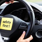Volante de un vehículo con un etiqueta amarilla pegada que dice seguridad primero.