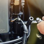 Primer plano de un compartimento de motor donde una persona manipula un componente con una llave inglesa.